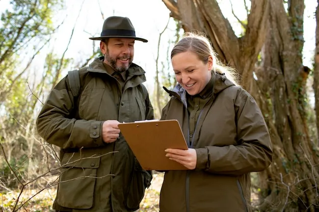 Two people in olive field jackets reading notes on a clipboard in woodland